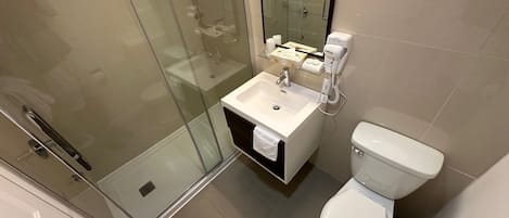A bathroom with a glass shower enclosure, a sink, a toilet, and a hairdryer.