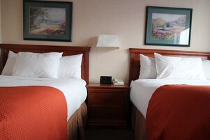 Habitación de hotel con dos camas, cada una con ropa de cama blanca y mantas rojas. Hay dos cuadros en la pared, una mesita de noche con una lámpara y un teléfono entre las camas.