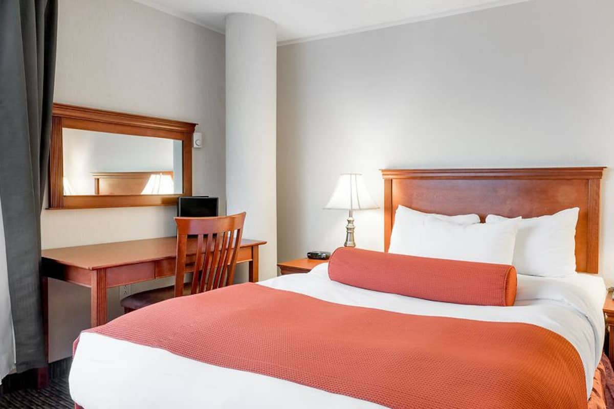 Una habitación de hotel con una cama grande, un escritorio, una silla, una mesita de noche y un espejo.