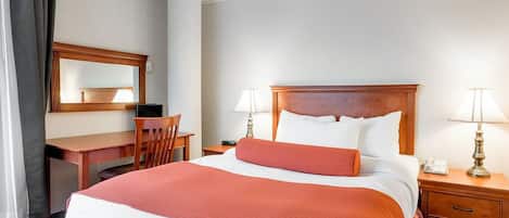 A hotel room with a large bed, a desk, a chair, a nightstand, and a mirror.