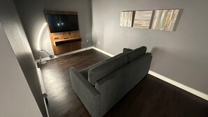 Un salón con un sofá gris, un televisor de pantalla plana montado en una pared de madera y una mesita auxiliar.