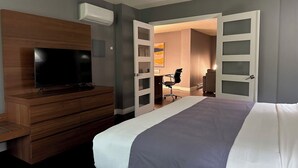 Una habitación de hotel con una cama, un televisor sobre un aparador de madera, y una puerta que da a un baño.