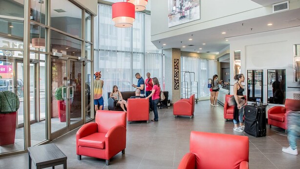 Un hall de hotel con asientos rojos, ventanas amplias y puerta de vidrio.