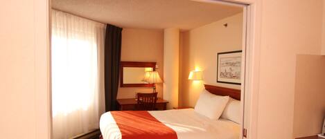 A hotel room with a bed, a desk, a chair, a lamp, and a framed picture on the wall.