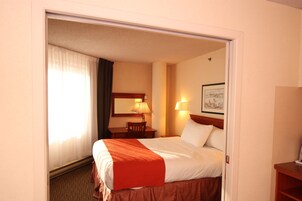 Une chambre d’hôtel avec un lit, un bureau, une chaise, une lampe et un tableau encadré au mur.
