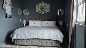 A bedroom with a tufted headboard bed, a large window with curtains, and a geometric-patterned rug. - Hotel Milenio (Nanacamilpa)