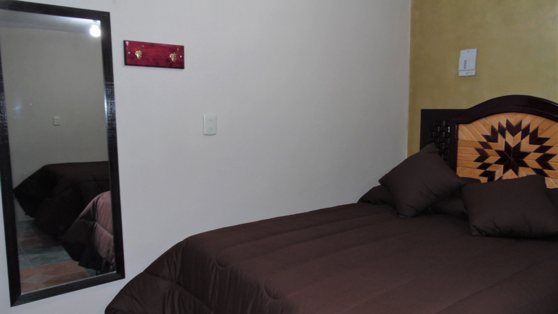 Une chambre avec un grand miroir, un lit doté d’une tête de lit à motifs géométriques et un élément décoratif rouge sur le mur.