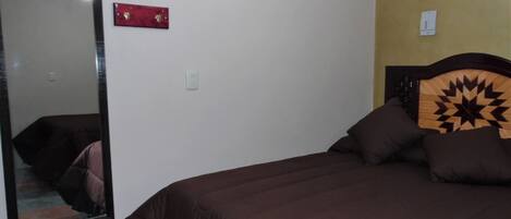 Une chambre avec un grand miroir, un lit doté d’une tête de lit à motifs géométriques et un élément décoratif rouge sur le mur.