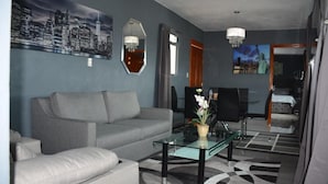 A modern living room with a grey sofa, a glass coffee table, and a cityscape painting on the wall. - Hotel Milenio (Nanacamilpa)