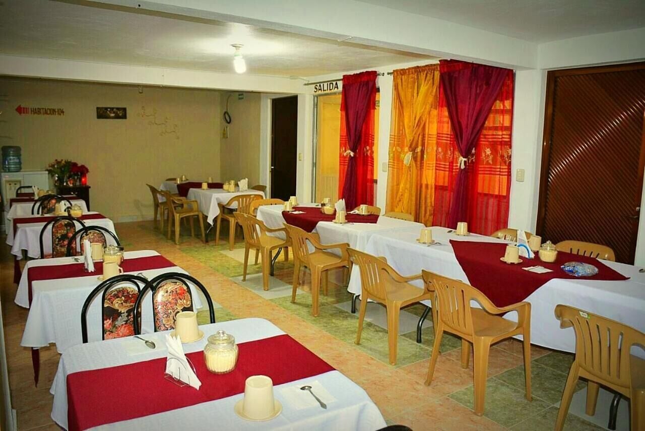 Un comedor con varias mesas dispuestas para el servicio, un cartel que indica la salida y una puerta con una cortina roja.