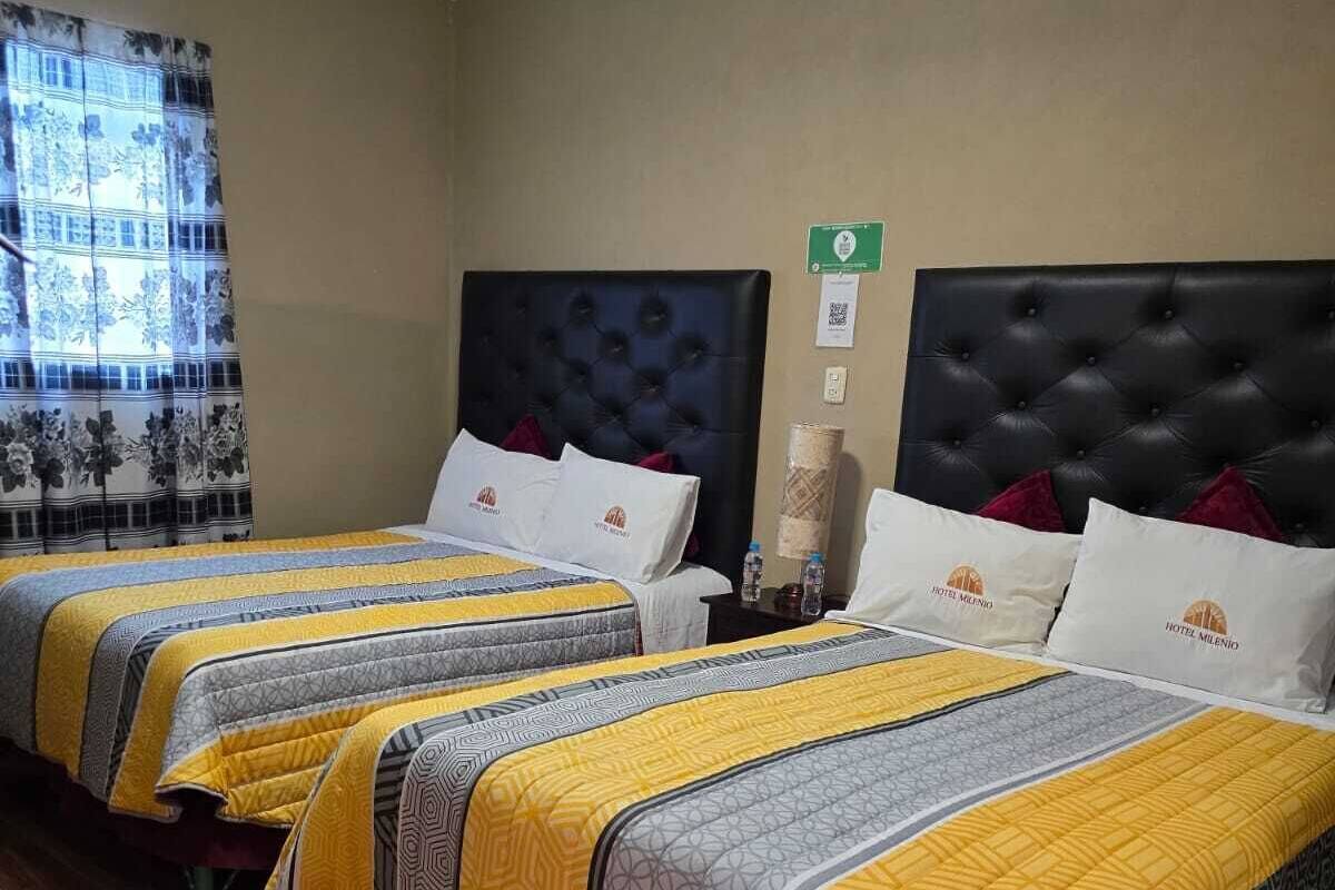 A hotel room with three beds, each with a headboard, a window with a curtain, and a wooden floor.