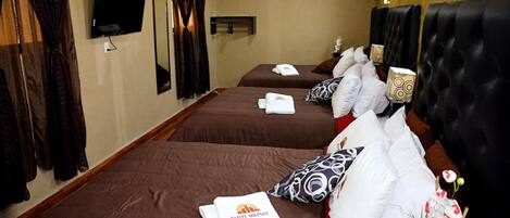 Quarto de hotel com duas camas, cada uma com um espalha roupa castanho e toalhas brancas. Há uma televisão na parede e uma janela com cortinas.