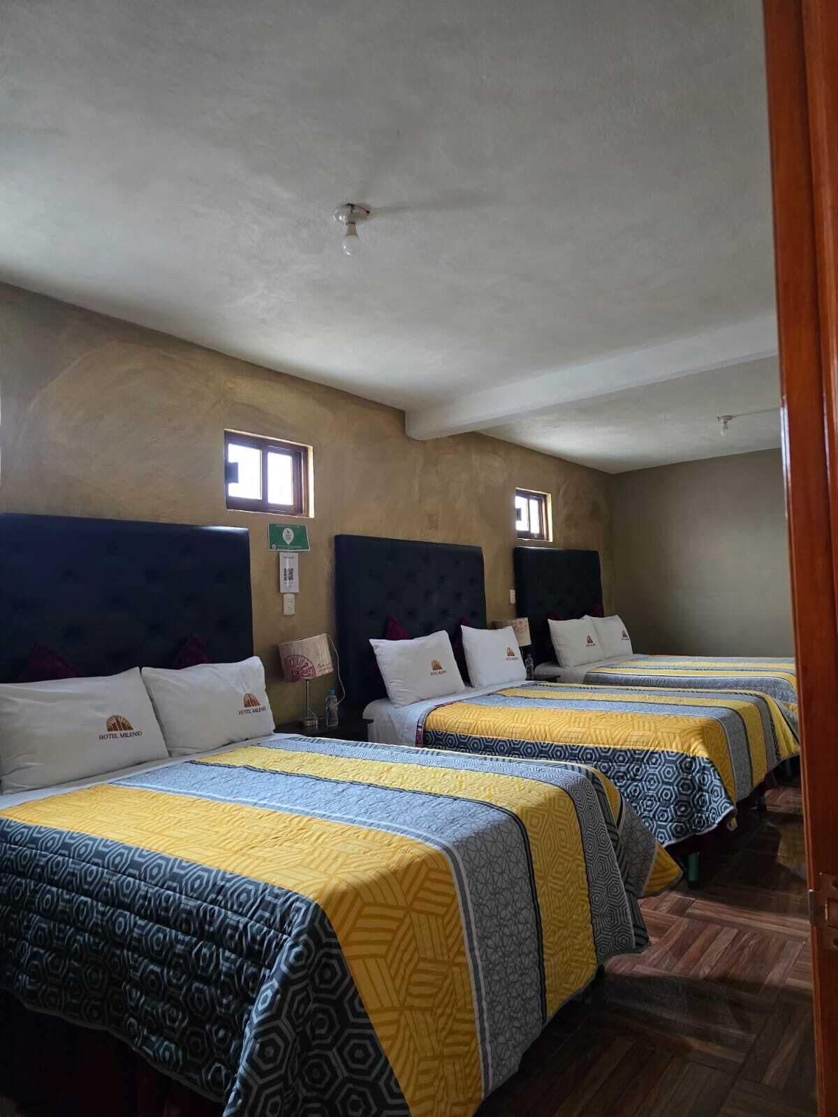 A hotel room with four beds, each with a headboard, a window, and a wall-mounted sign.
