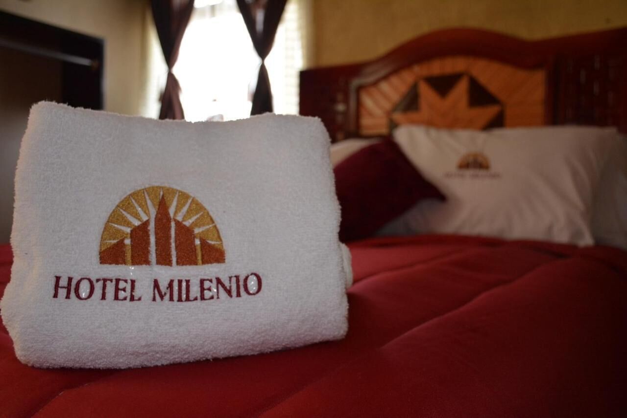 A hotel towel with the logo and name "HOTEL MILENIO" on a bed with a red bedspread.