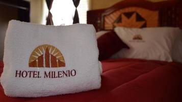 A hotel towel with the logo and name "HOTEL MILENIO" on a bed with a red bedspread.