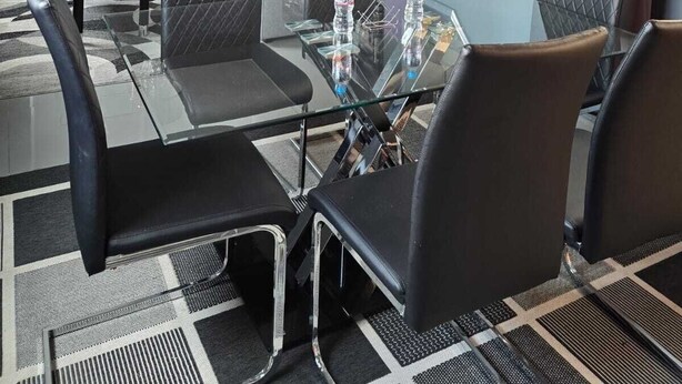 A modern hotel room with a glass dining table, black leather chairs, a cityscape painting, and a chandelier. - Hotel Milenio (Nanacamilpa)
