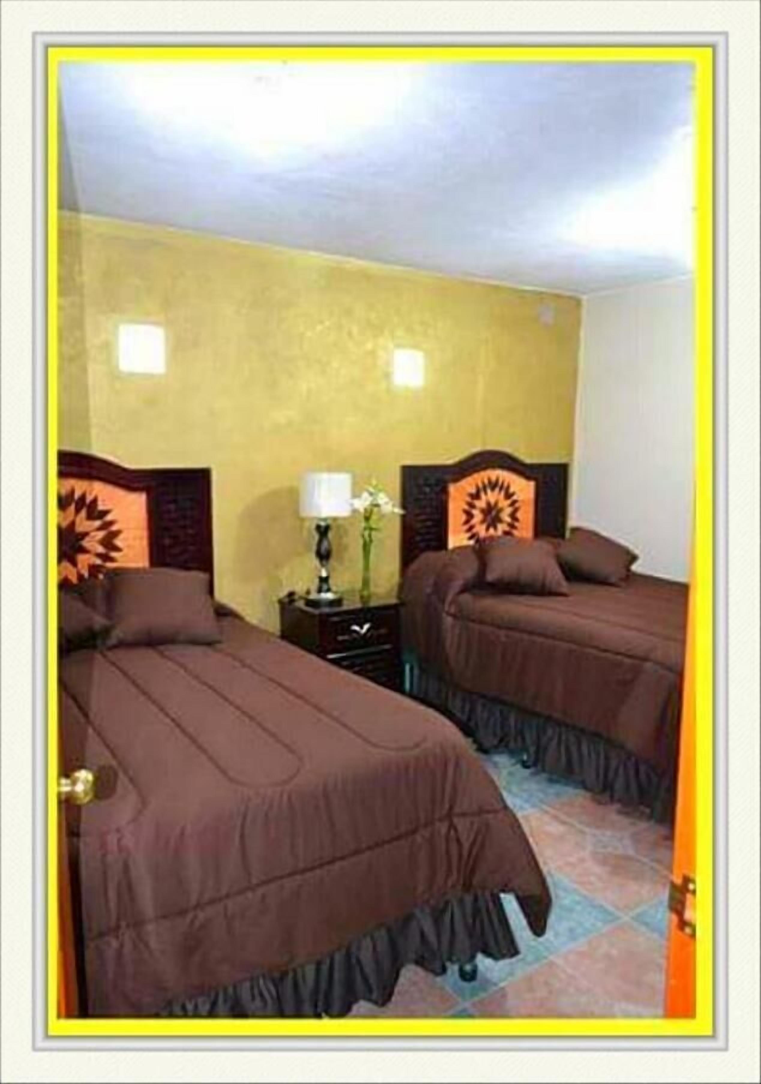 Una habitación con dos camas, cada una con cabecera y mesita de noche con lámpara.