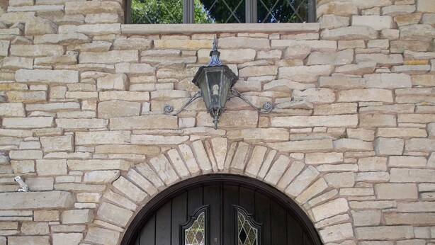 Un bâtiment en pierre avec une porte double en bois sombre, une petite fenêtre au-dessus de la porte et deux paniers de fleurs de chaque côté de la porte.