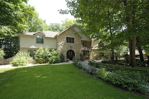 A two-story house with a stone facade, a front lawn, and a variety of plants and shrubs. - The Roost Bed and Breakfast (Appleton)