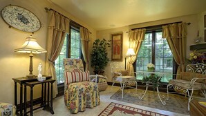 Une pièce chaleureuse avec des motifs floraux sur les meubles, une table ronde avec une lampe et une grande fenêtre avec des rideaux.