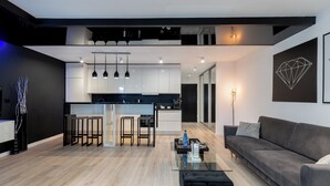 Een moderne woonkamer met een glazen salontafel, een grijze bank en een keuken op de achtergrond.