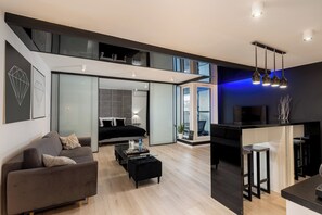 Uma sala de estar moderna com sofá, mesa de centro e televisão. Escada leva a um andar superior.