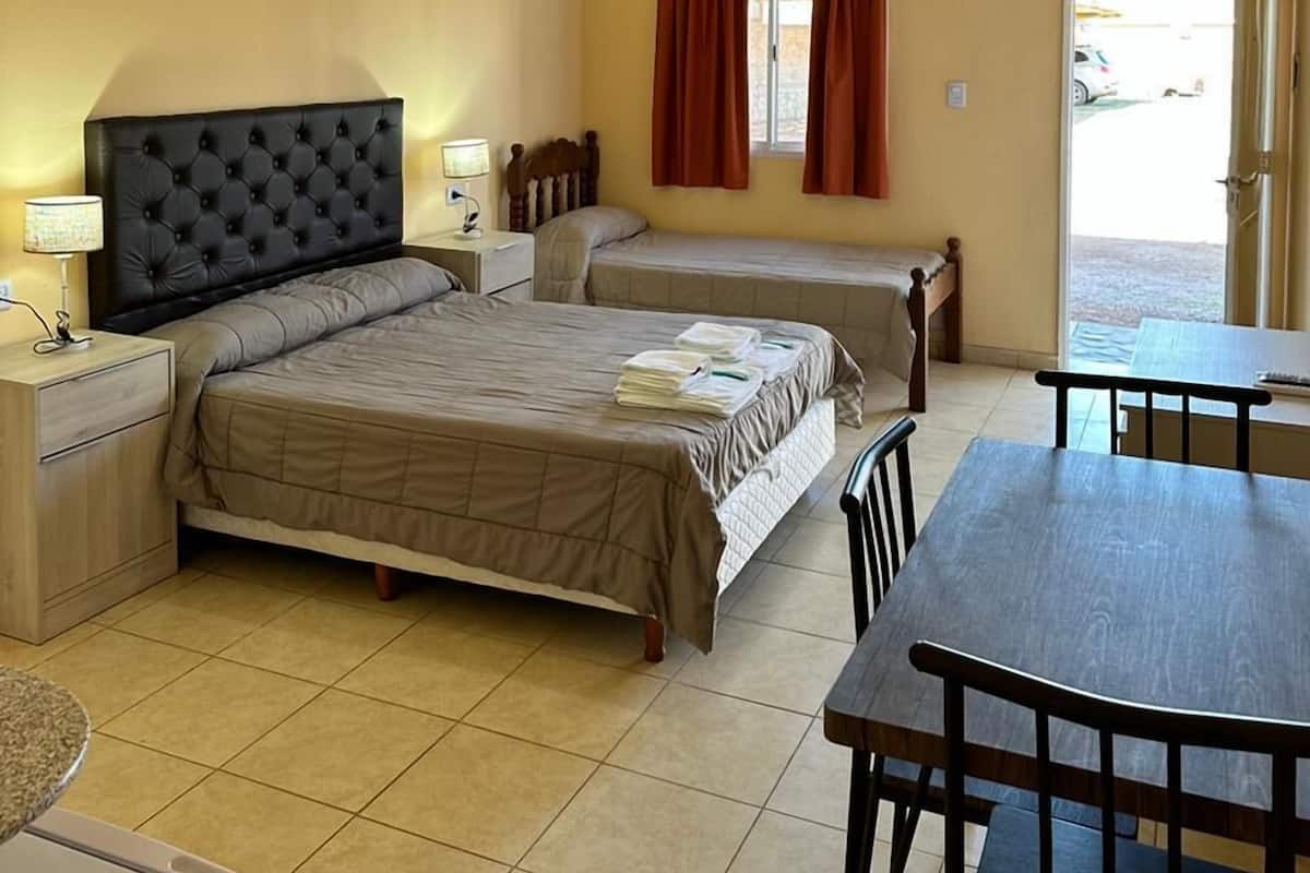 A hotel room with a large bed, a smaller bed, a desk with a chair, a table, and a TV.