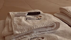 A neatly made bed with a dark headboard, a folded white towel with text, and a small item on the bed.