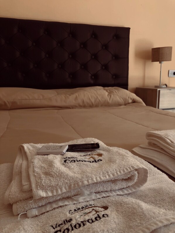 A neatly made bed with a dark headboard, a folded white towel with text, and a small item on the bed.