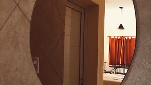 A circular mirror reflecting a room with a door, a bed, and a hanging light fixture.