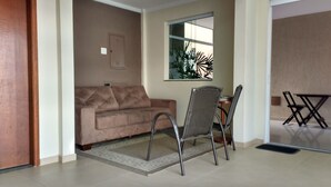 Un salon avec un canapé beige, une table à manger avec des chaises et une fenêtre agrémentée d’une plante.
