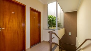 Un couloir avec deux portes en bois, une rambarde en verre et une plante en pot.