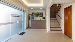 Un espace d’accueil d’hôtel avec un comptoir, un tableau accroché au mur et un escalier menant à l’étage supérieur.