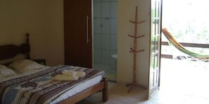 A bedroom with a bed, a wooden door, a shower, and a hammock outside. - Pousada dos Tucanos (Sao Thome das Letras)