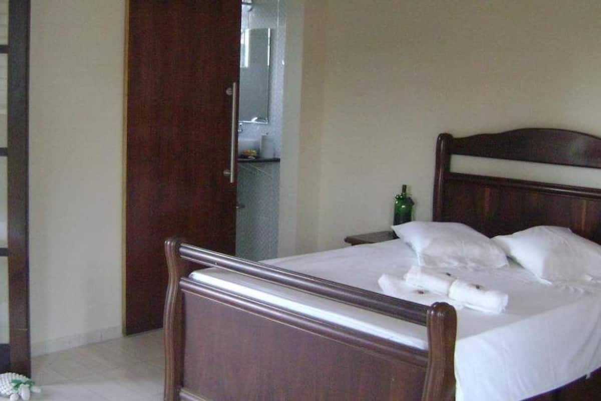 A neatly made bed with white linens and pillows, a wooden headboard, and a bedside table with a green bottle.