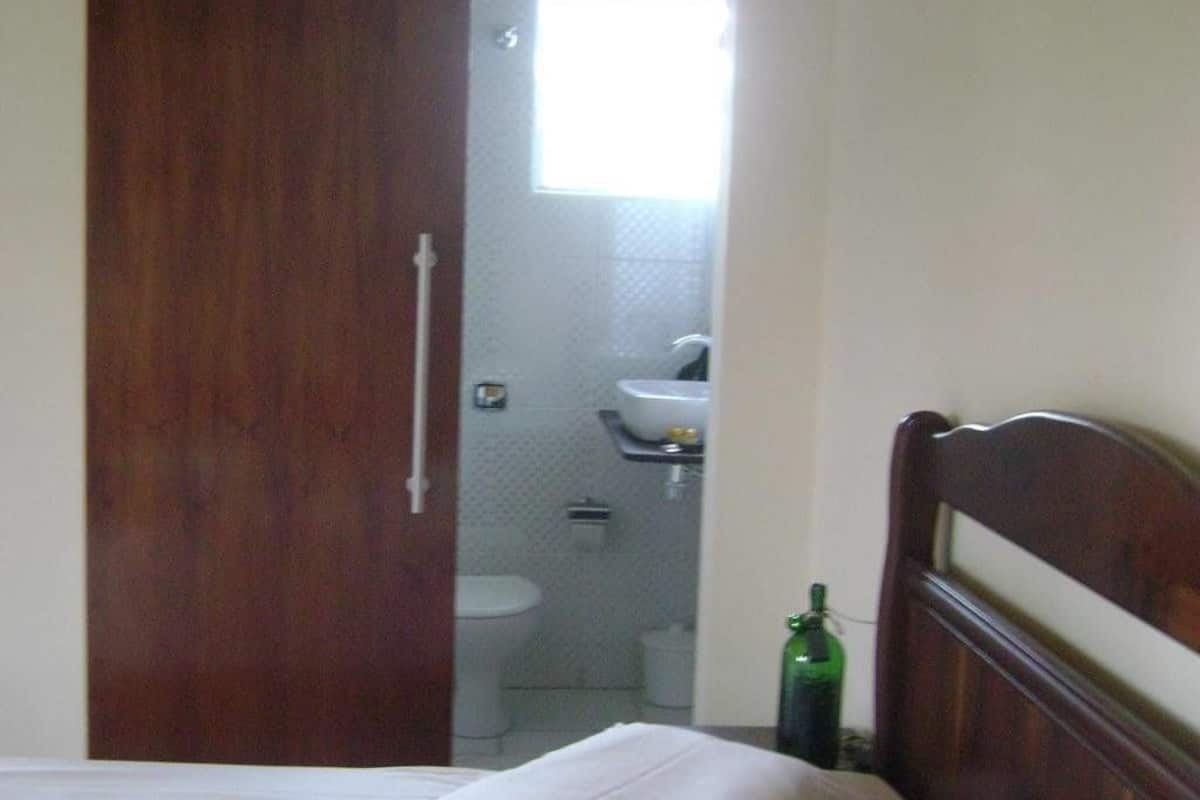 A bedroom with a wooden headboard, a bed with white bedding, and a green bottle on the nightstand.
