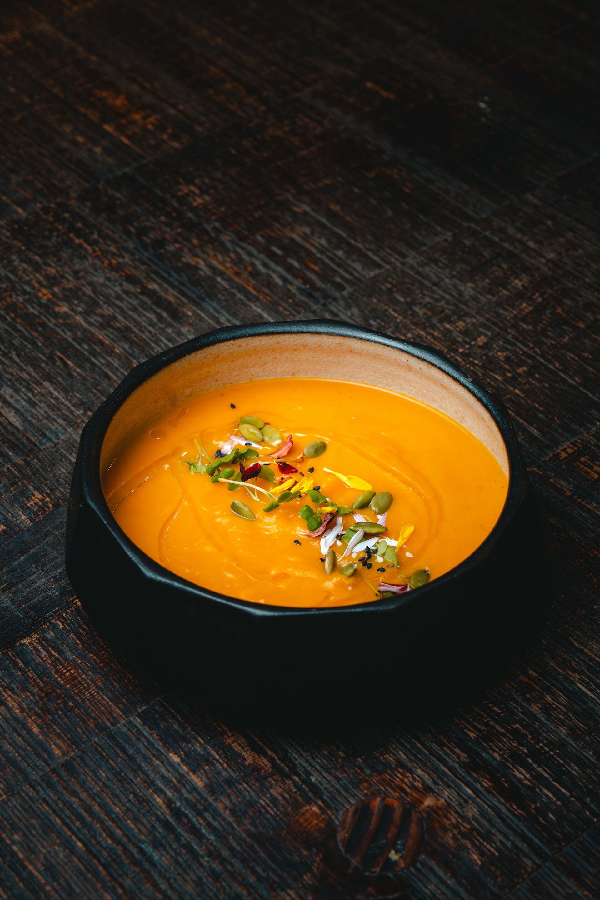 A bowl of soup with seeds and herbs on a wooden surface.