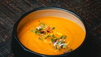 A bowl of soup with seeds and herbs on a wooden surface.