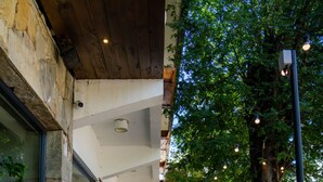 Une allée dallée bordée de murs en pierre, avec un plafond en bois et des luminaires suspendus.