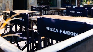 Un espace extérieur aménagé avec des tables et des chaises portant l’inscription « Stella Artois », une façade en pierre et une enseigne indiquant « Casa Chola Restaurante ».