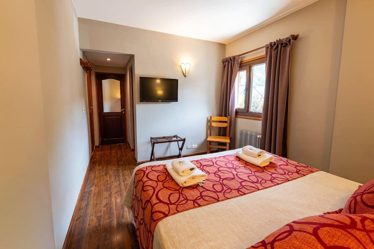 A hotel room with a bed, a TV, a chair, and a window with curtains.