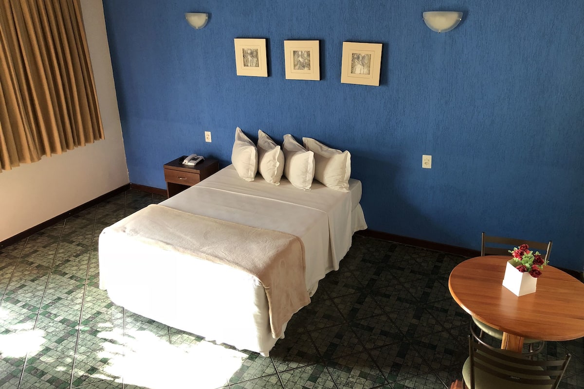 Una habitació d'hotel amb un llit, una tauleta de nit, una taula amb flors i llums penjades a la paret.