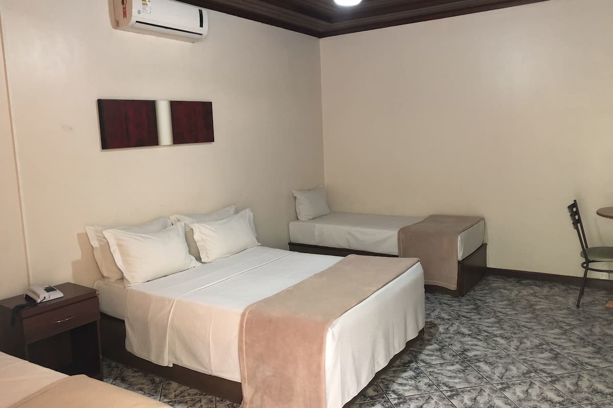 Habitació d'hotel amb un llit, una taula de nit, una cadira, una taula petita i un aparell d'aire condicionat.