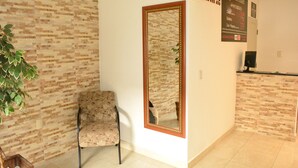 Zona de recepción de hotel con pared de ladrillo, un espejo grande, mostrador de recepción y una silla.