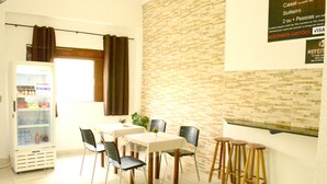 Un comedor con pared de ladrillo, un refrigerador lleno de bebidas y un cartel con el menú.