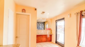 A hotel room with a marble countertop, a wooden bench, a tiled floor, a door, a window with curtains, and a view of the street. - Crown Inn (Denver City)