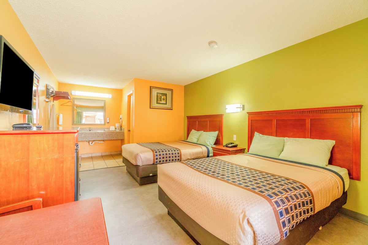 A hotel room with two beds, a TV, a desk, and a bathroom.