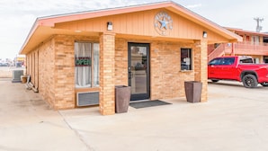A small brick building with a "Welcome" sign, a black door, and a red truck parked in front. - Crown Inn (Denver City)