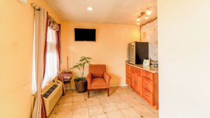 A compact kitchen with a built-in oven, a small dining area with a chair, a potted plant, and a flat-screen TV mounted on the wall. - Crown Inn (Denver City)