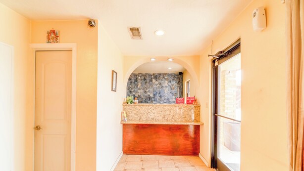A hallway with a door, a counter with a stone backsplash, and a window with a view. - Crown Inn (Denver City)